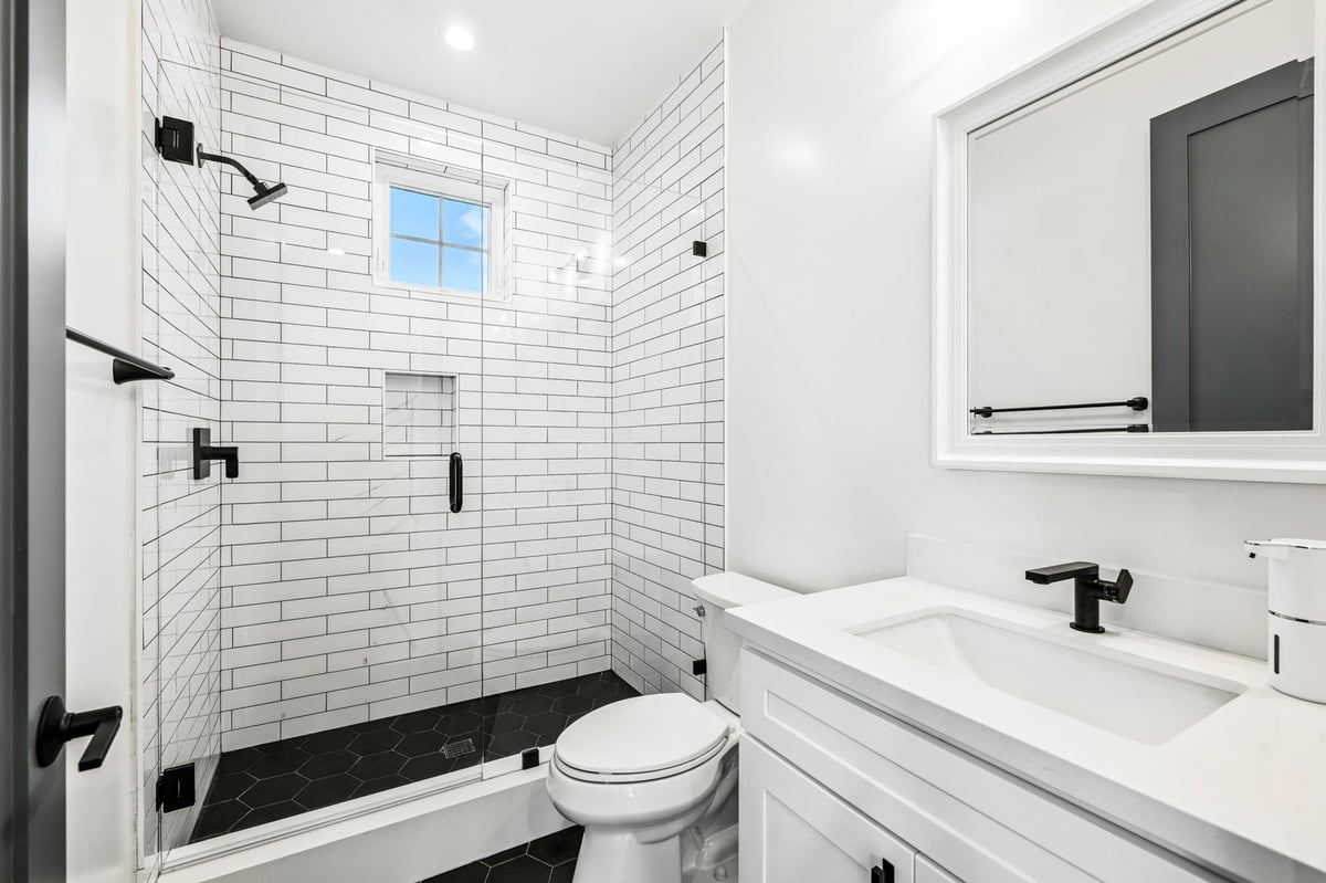 Modern white bathroom with subway tiles, black fixtures, and glass shower door