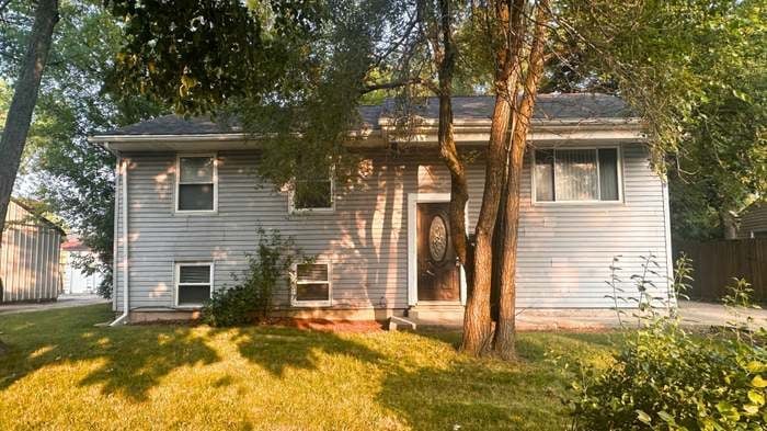 Two-story white vinyl siding house with large front trees and green lawn, surrounded by shade