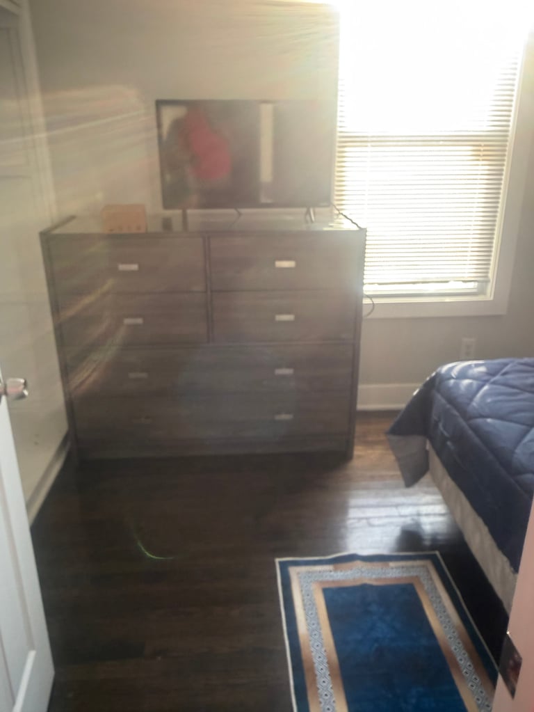 Bedroom interior with dark wood dresser topped with flat-screen TV, blue patterned rug, and bed visible on right side