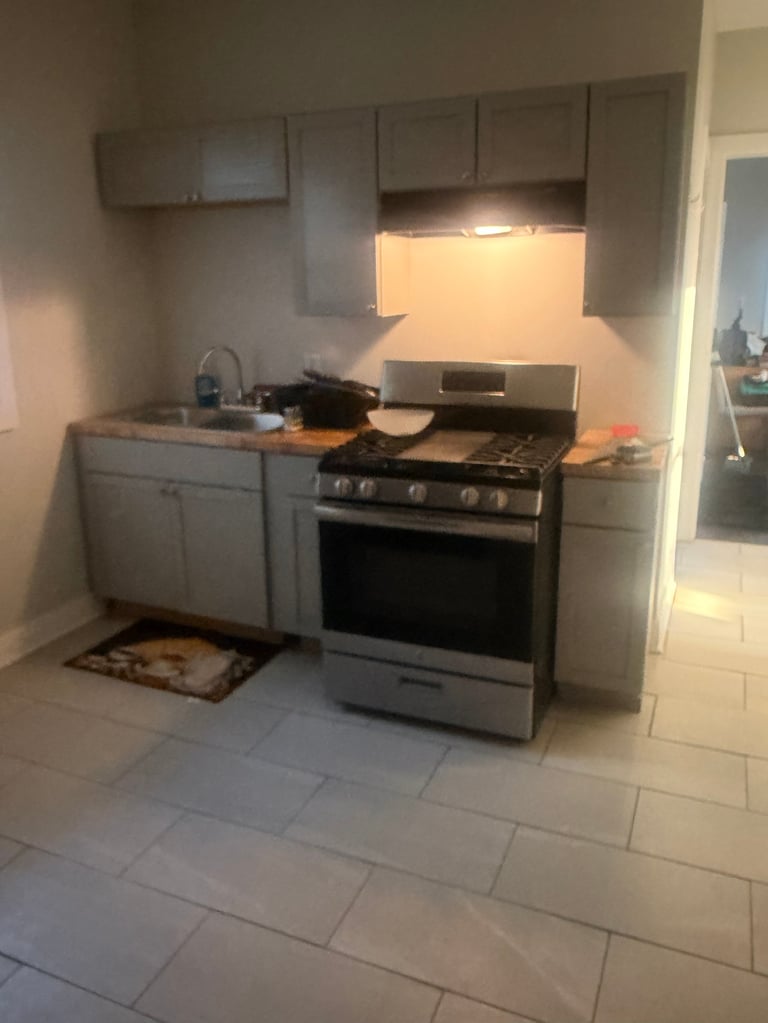 Modern kitchen with gray cabinets, stainless steel stove and oven, tile countertop, under-cabinet lighting, and brown door mat