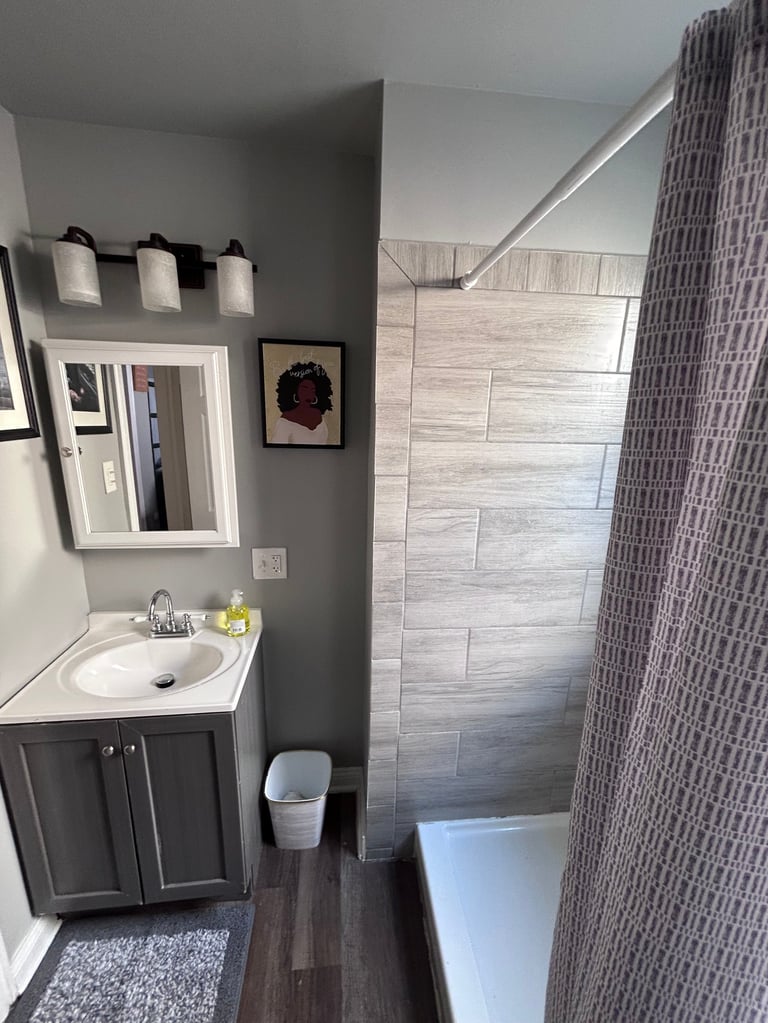 Modern bathroom with gray walls, vanity with white sink, framed mirror, toilet, and walk-in shower with tile surround