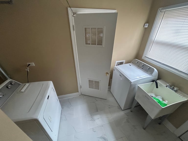 Small laundry room with washing machine, dryer, utility sink, and open door with white trim