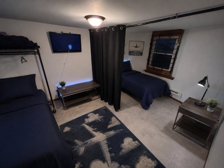Modern dorm room with two twin beds separated by black curtain, desk, nightstands, and geometric patterned rug