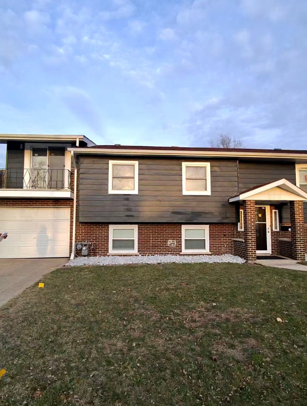 Two-story brick and wood sided house with attached garage, front lawn, and clear sky in background