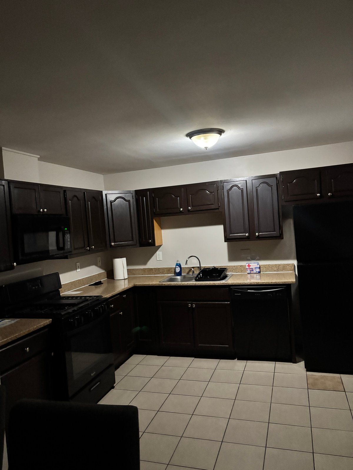 Modern kitchen with dark cabinets, beige countertops, tile flooring, and stainless steel appliances